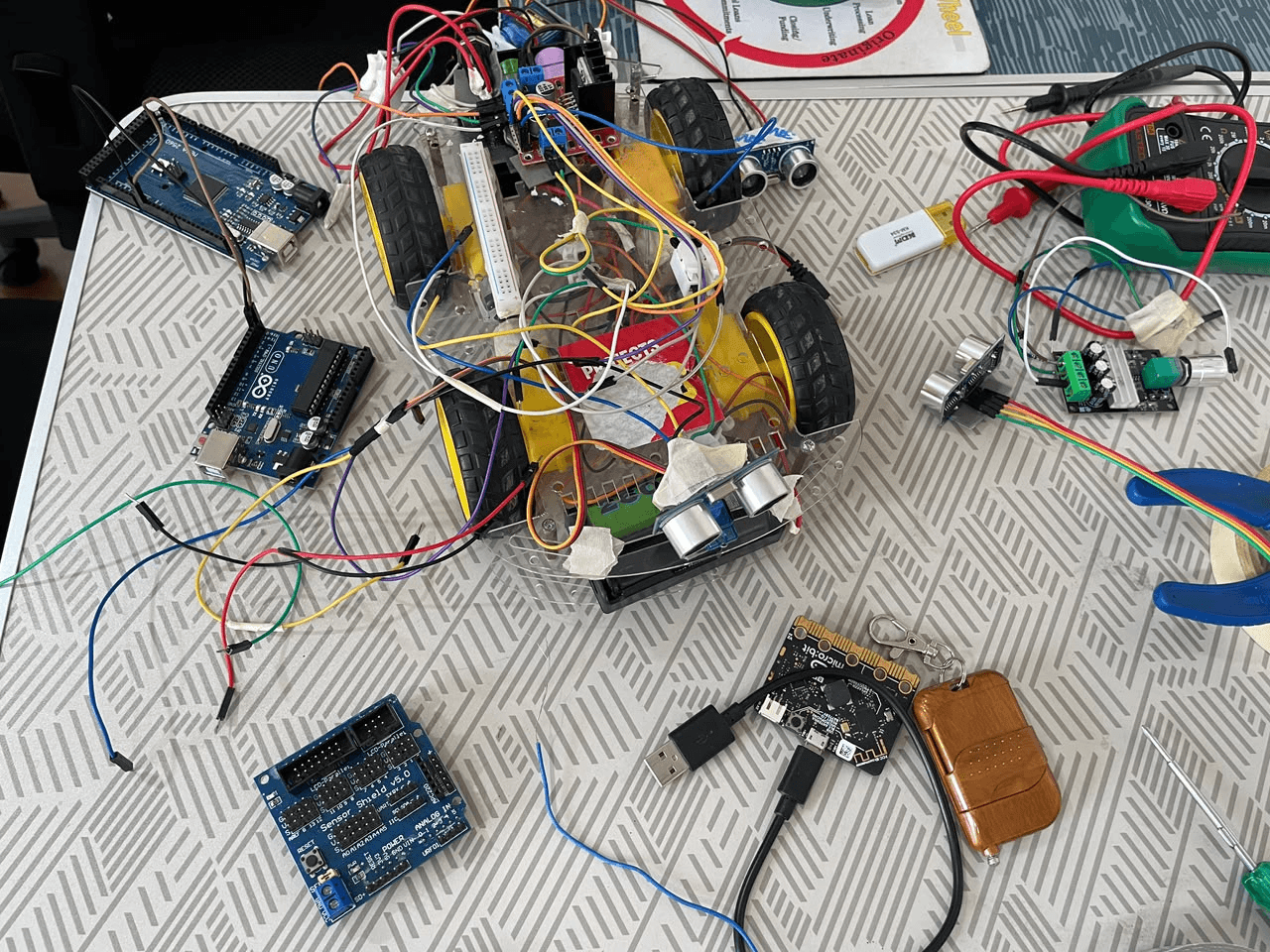 A four-wheeled robot car with ultrasonic sensors, Arduino boards and a micro:bit on the bench.