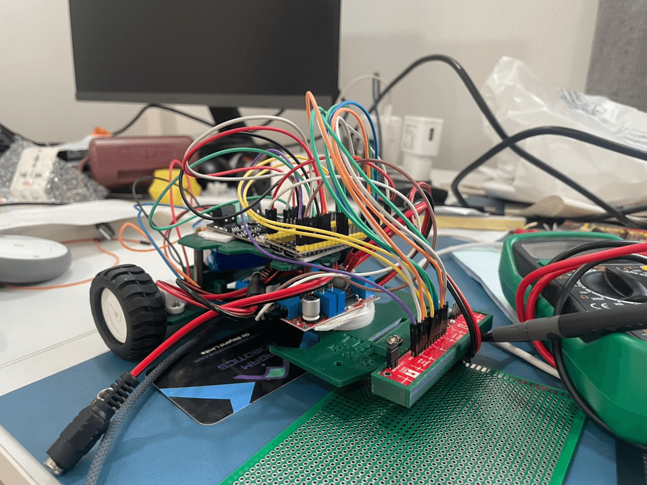A hand-wired robot build on a 3D-printed chassis, mid-debug with a multimeter.