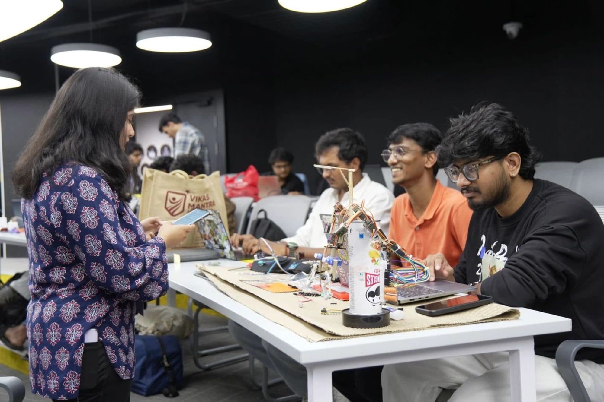 Builders at a table with a servo-driven arm prototype, laptops open.