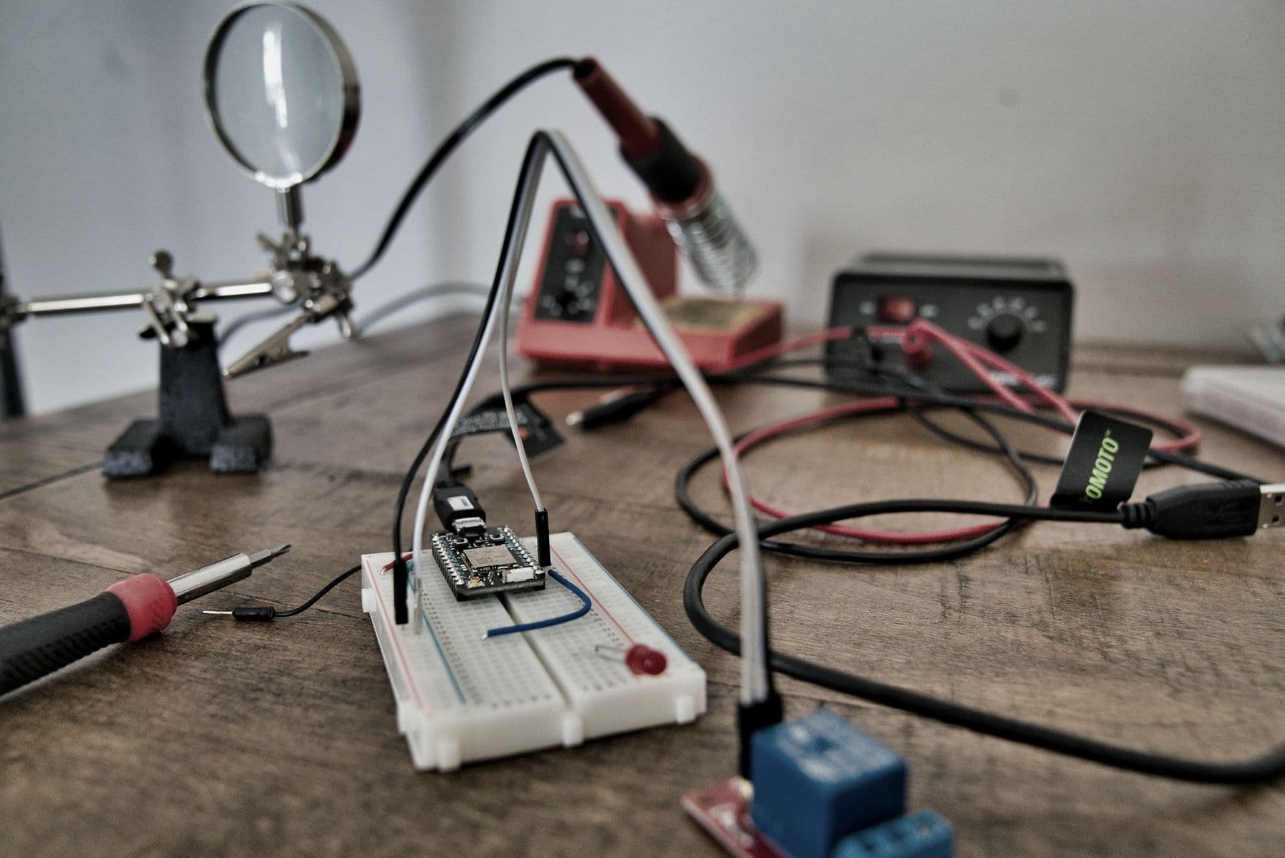 A workbench with a soldering station, helping hands with a magnifier, and a breadboard prototype.